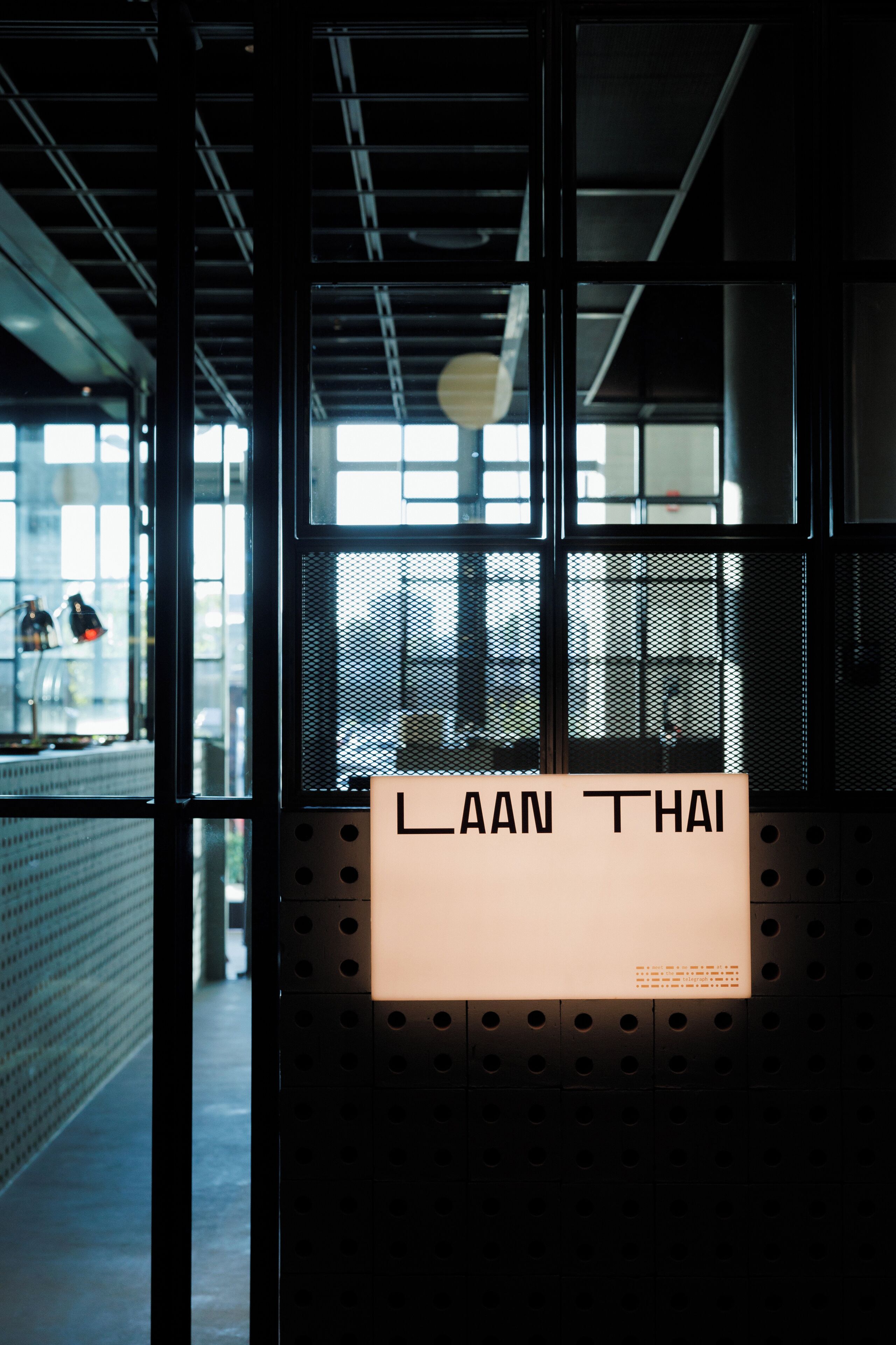 Une porte surmontée d’une enseigne indiquant « LAAN THAI », donnant sur un intérieur moderne avec de grandes fenêtres et des éléments de style industriel.