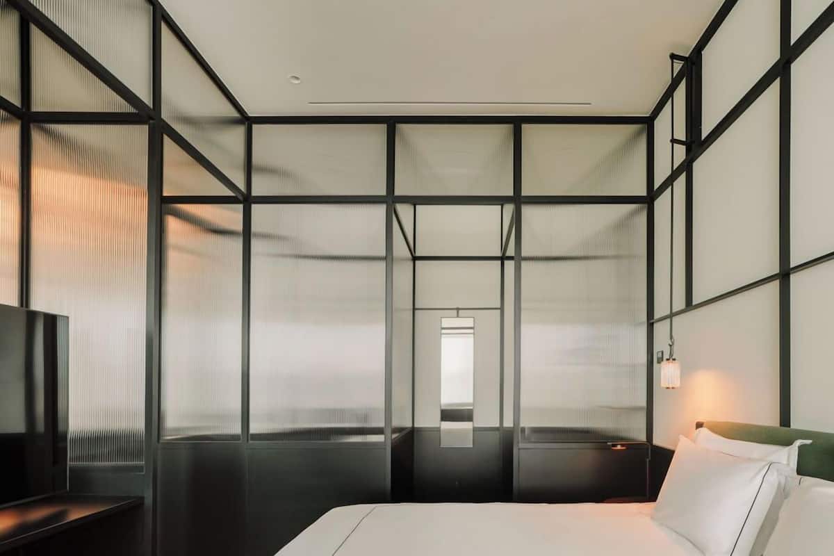 A modern hotel room with a large bed, a TV on a stand, and a view through a large window.