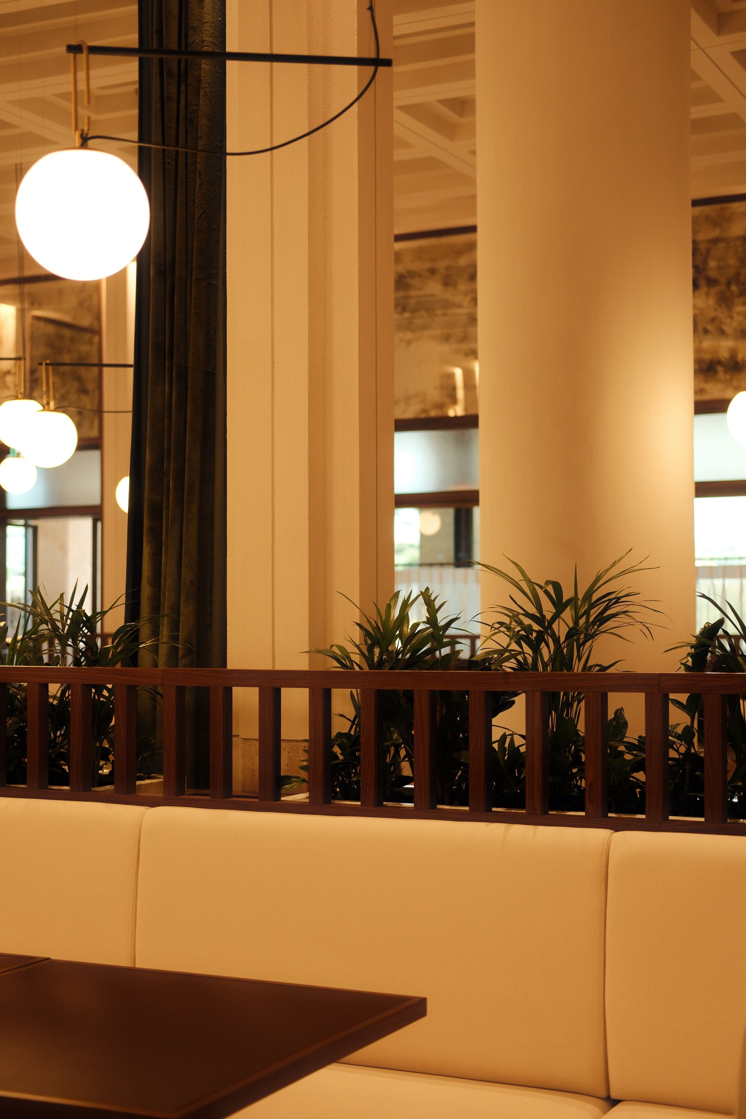 Un espace détente avec une table en bois et des bancs rembourrés, entouré de plantes en pot et éclair é par des lampes sphériques suspendues.