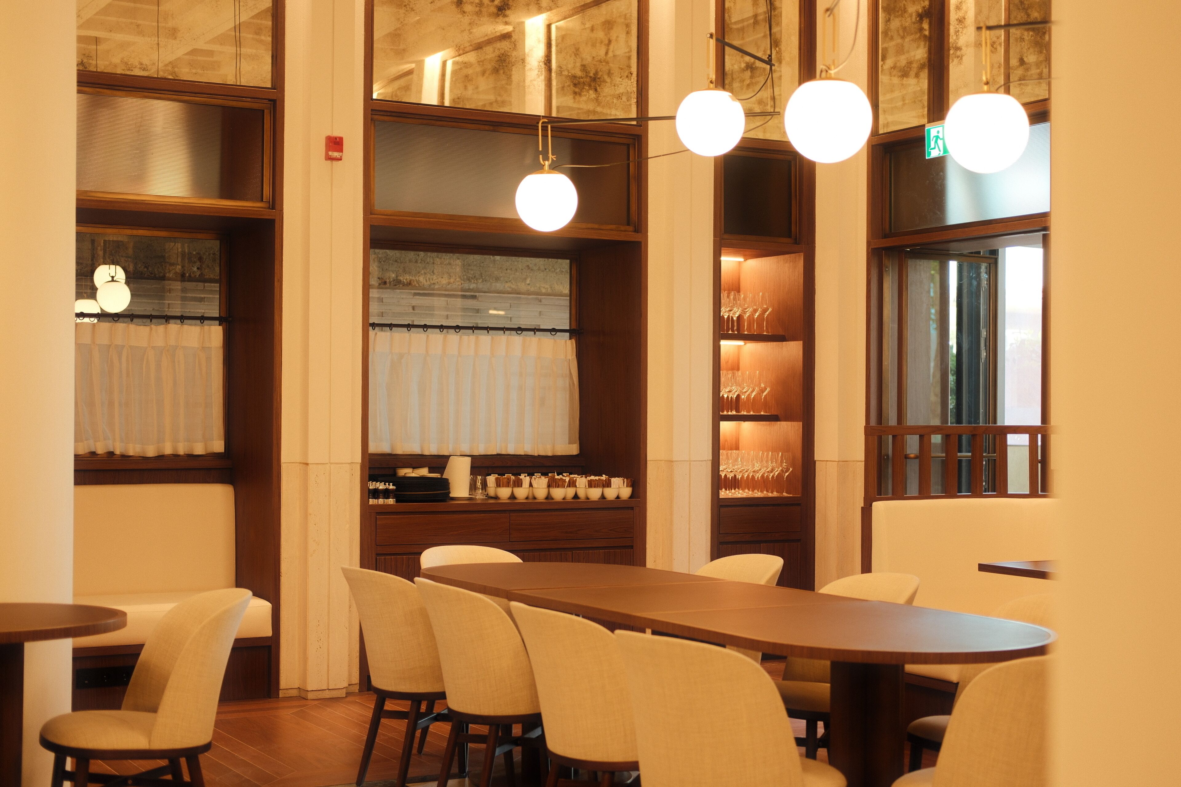 A restaurant with a long wooden table, several chairs, and hanging spherical lights.