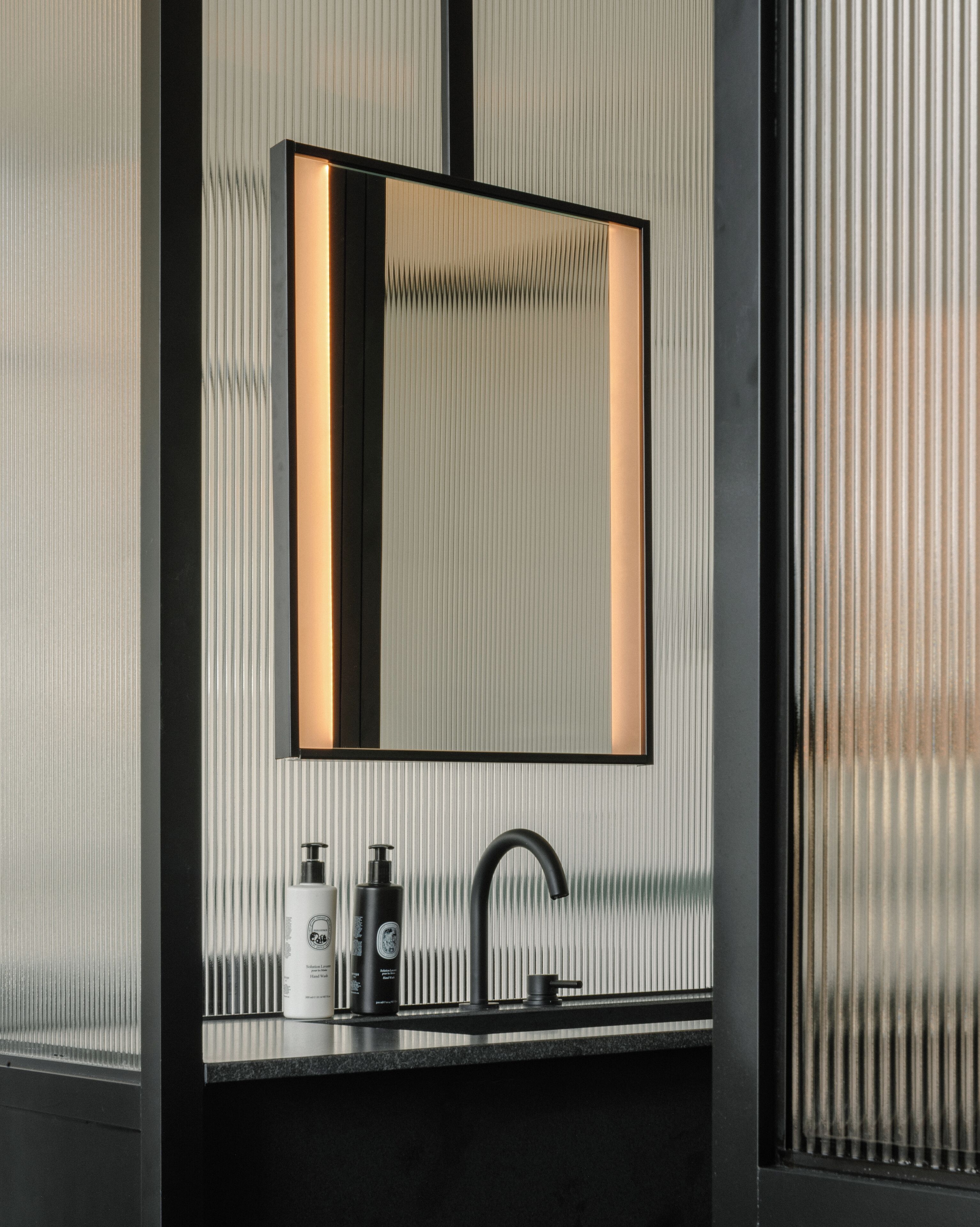 A modern bathroom with a black sink, a large mirror, and two bottles of hand soap.