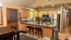 Una cocina con gabinetes de madera, encimeras de granito, electrodomésticos de acero inoxidable y un comedor con mesa y sillas.
