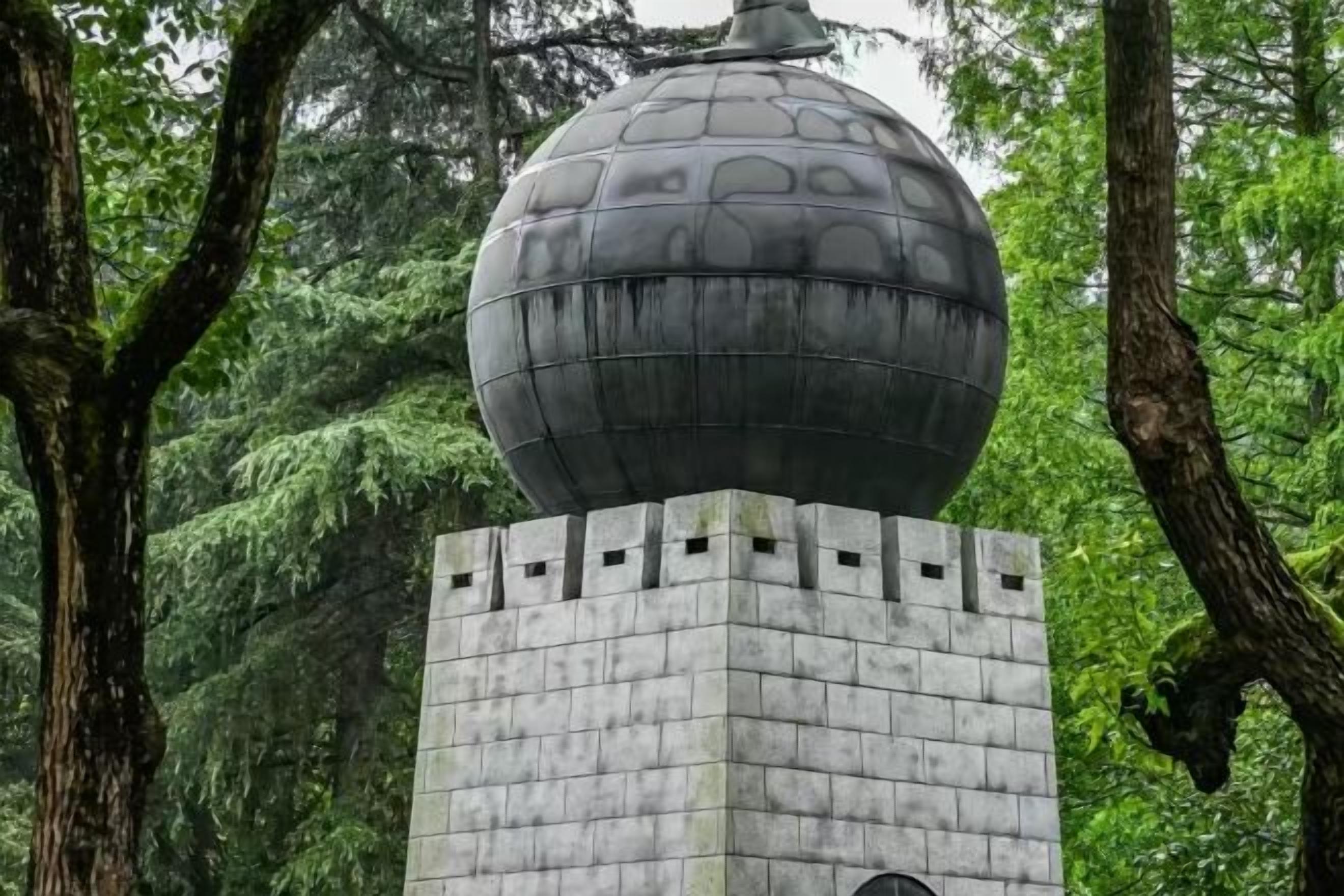 Un monumento sferico su una base quadrata, circondato da alberi.