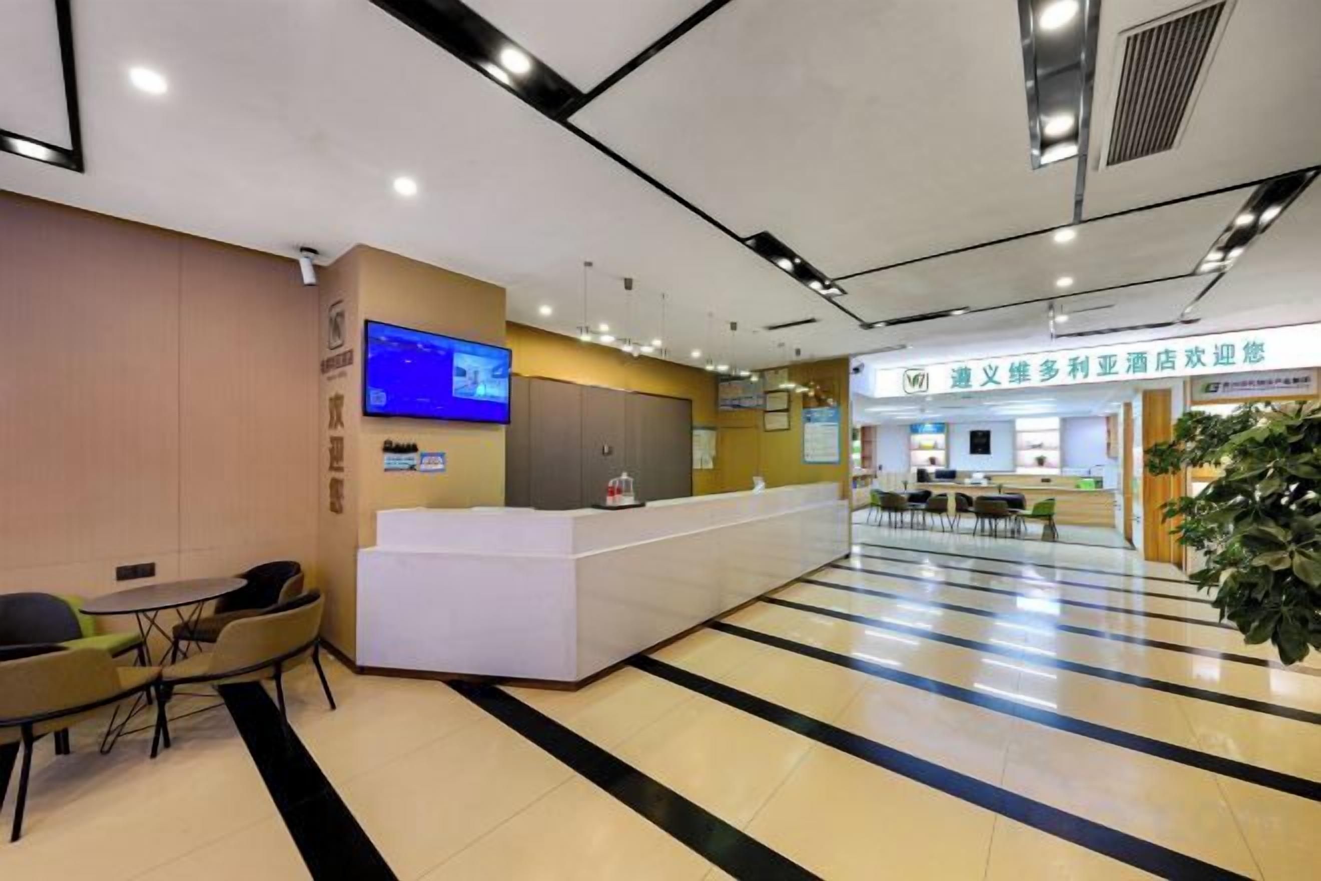 A hotel reception area with a reception desk, a television mounted on the wall, and a seating area with tables and chairs.