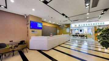 A hotel reception area with a reception desk, a television mounted on the wall, and a seating area with tables and chairs.