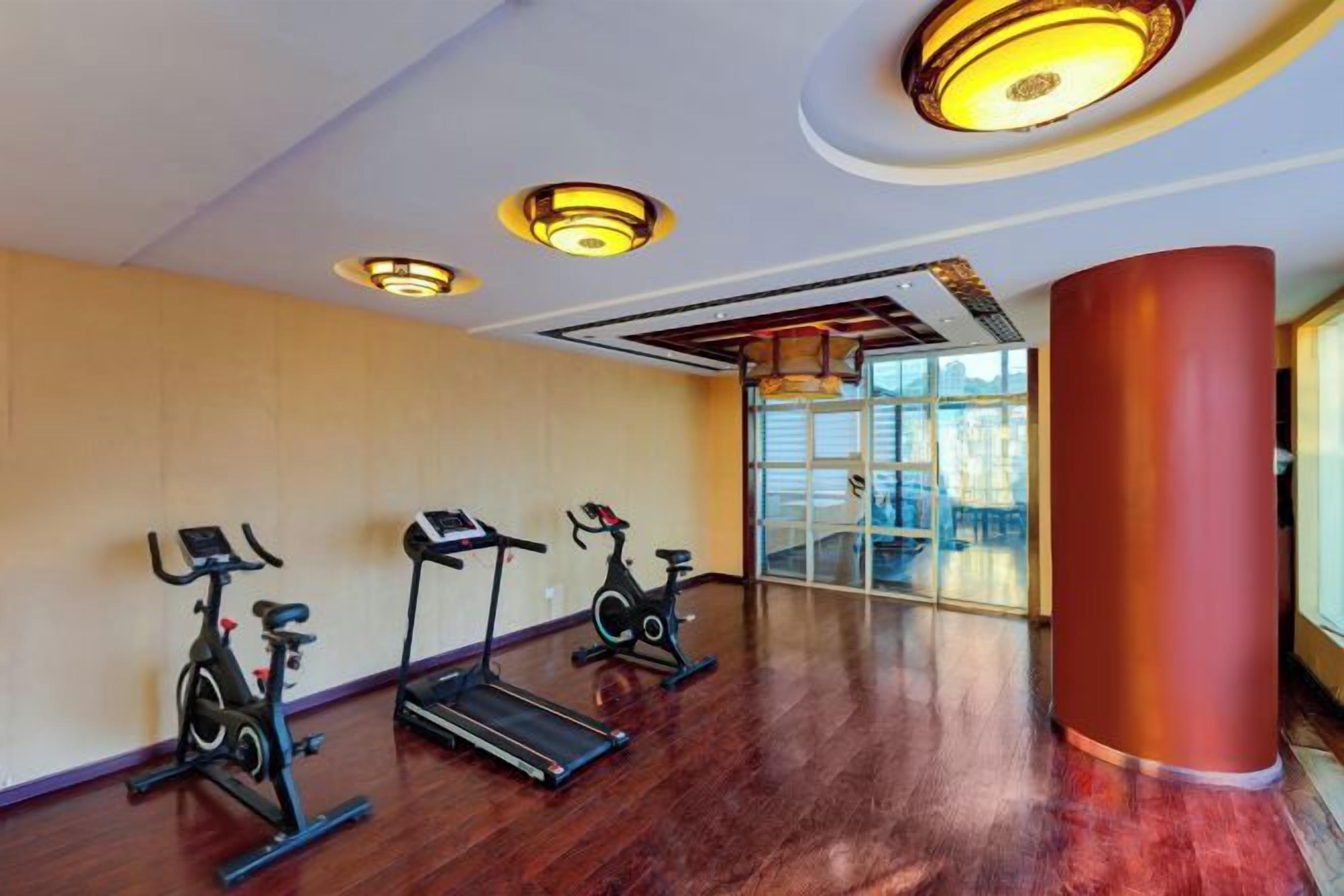 A gym with three stationary bikes and a treadmill, large windows, and a red pillar.