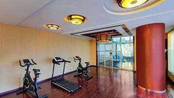 A gym with three stationary bikes and a treadmill, large windows, and a red pillar.