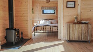 Un dormitorio acogedor tipo cabaña de madera, con cama, un armario de madera y un estufa de leña.