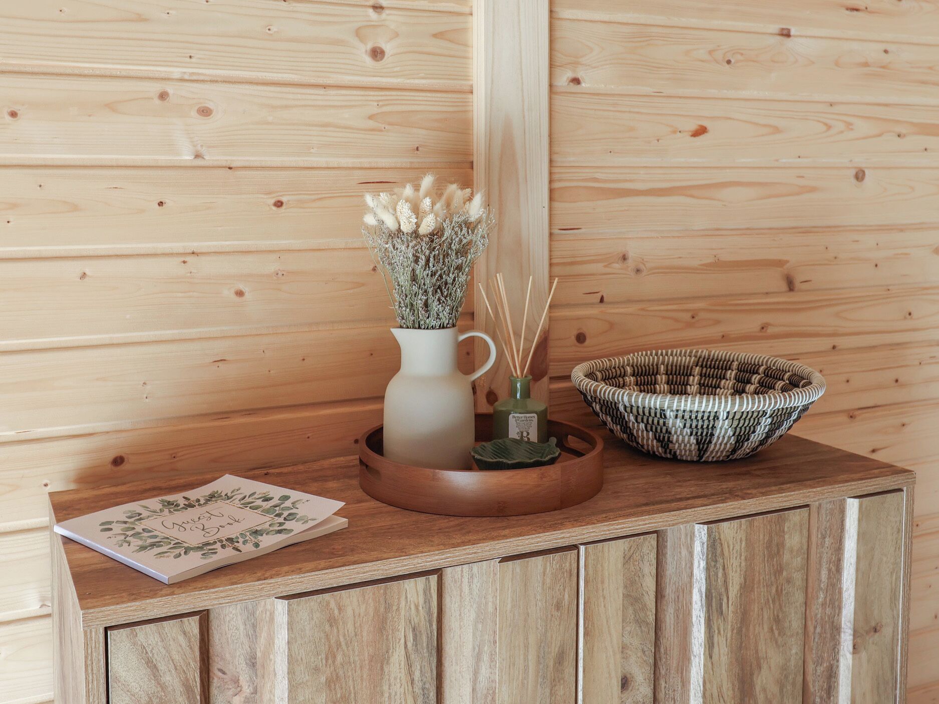 A wooden cabinet with a woven basket and a vase with dried flowers.