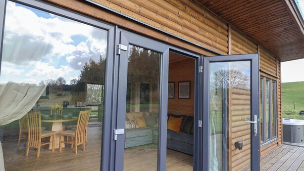 Una cabaña de madera con amplias puertas correderas de vidrio que dan a un espacio exterior con mesa y sillas.