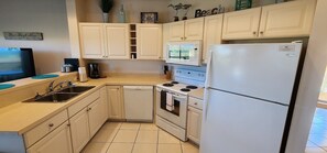 A compact kitchen with white cabinets, a dishwasher, a stove, and a refrigerator.