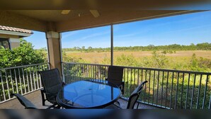 A balcony with a glass table and chairs, overlooking a grassy field.