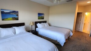 A hotel room with two beds, a nightstand with a lamp, and two paintings on the wall.
