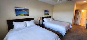 A hotel room with two beds, a nightstand with a lamp, and two paintings on the wall.