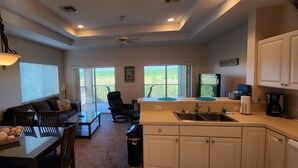 A modern kitchen with a dining area, a sofa, and a ceiling fan.