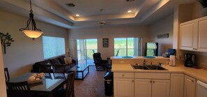 A modern kitchen with a dining area, a sofa, and a ceiling fan.