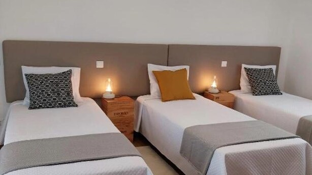 Een hotelkamer met drie eenpersoonsbedden, elk voorzien van een ander patroon kussen en een nachtkastje met een lamp.
