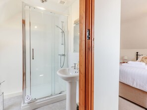 A modern bathroom with a glass-enclosed shower, a white sink, and a wooden door. - Robin's Nest (Craven Arms)