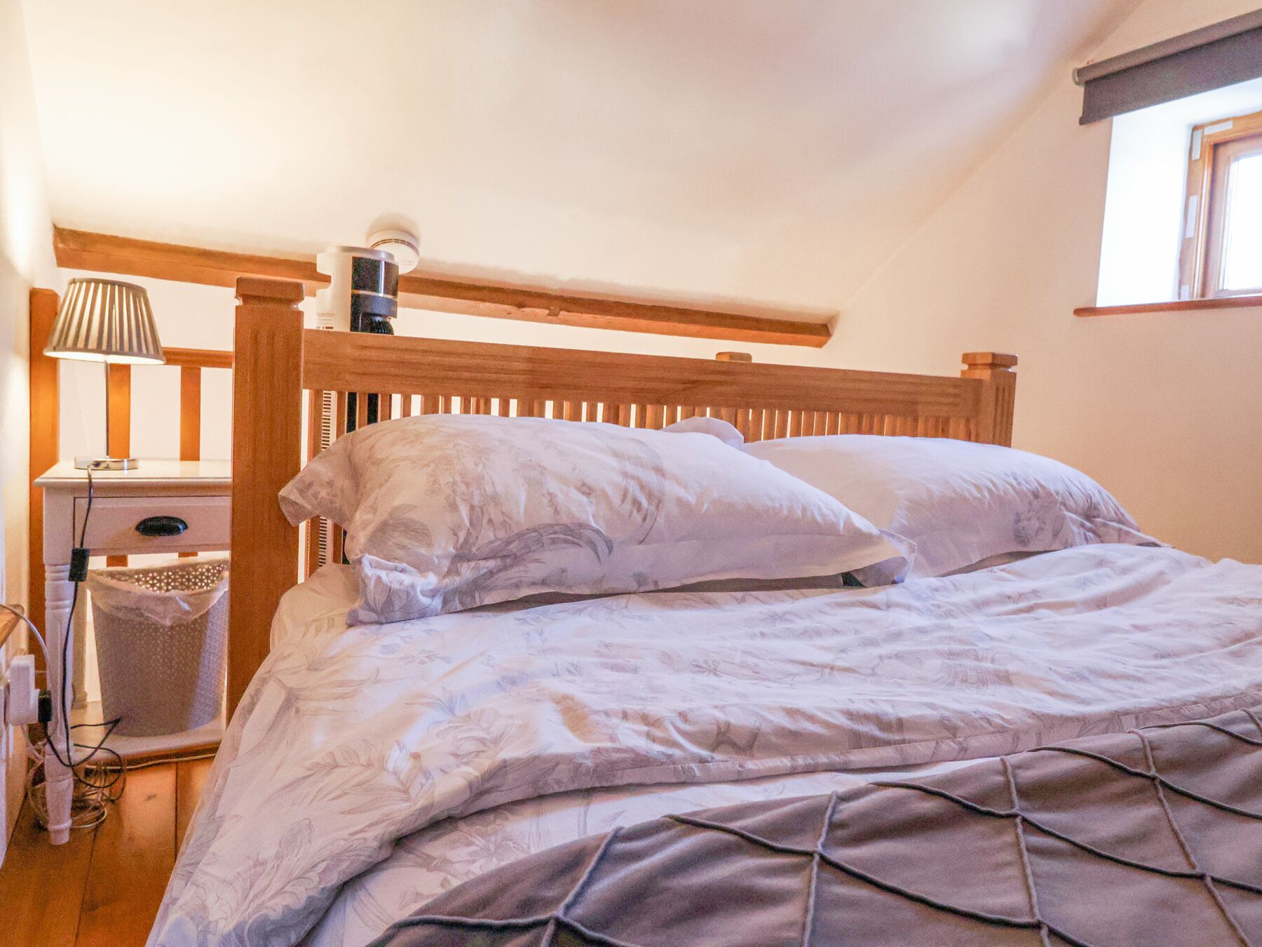 Un dormitorio con cabecera de madera, una mesita de noche con lámpara y una ventana con vistas.