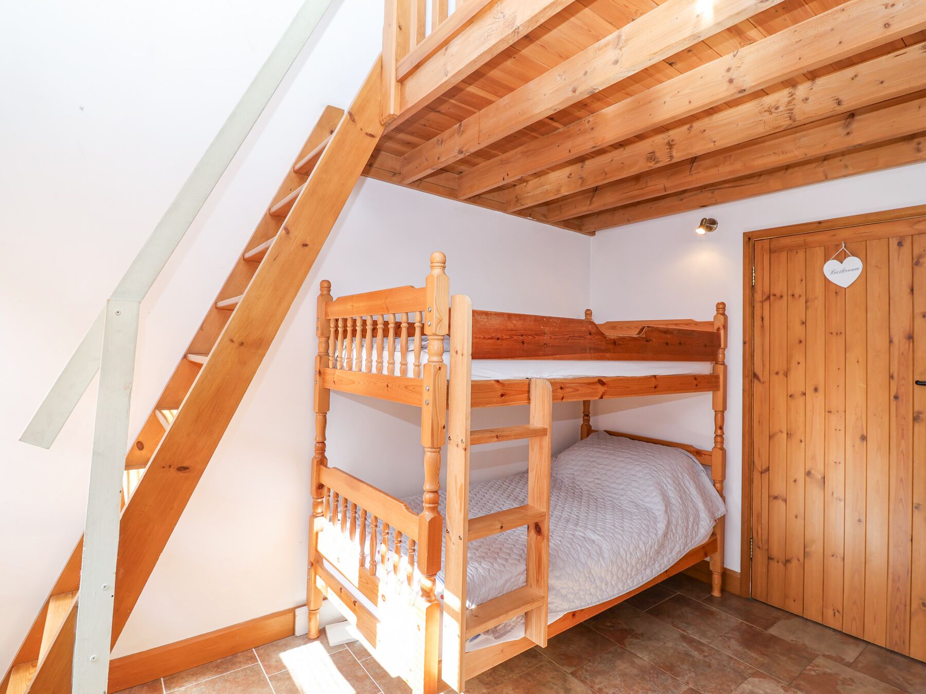 Ein Etagenbett in einem Zimmer mit geneigter Decke und einer Holztür mit der Aufschrift "Bad".