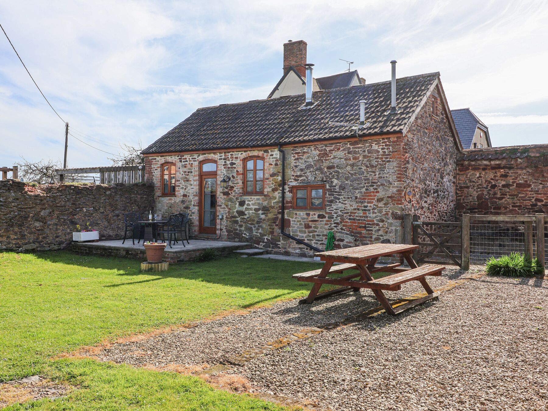 A stone building with a tiled roof, a wooden bench, and a gravel area.