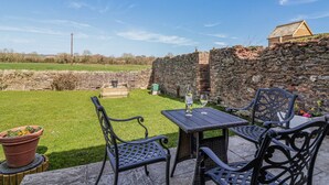 An outdoor patio with a stone wall, a wooden table, and two chairs. - The Yarde Annexe (Taunton)