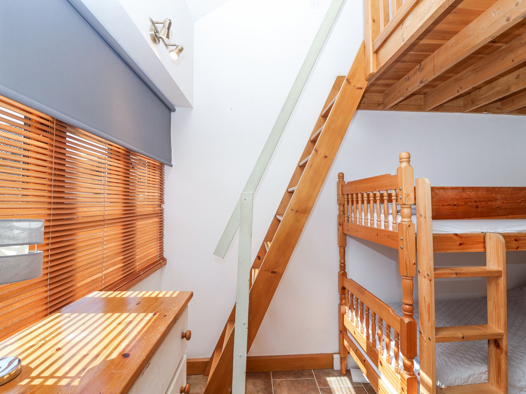 A room with a bunk bed, wooden furniture, and a sloped ceiling.