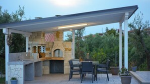 An outdoor kitchen with stone countertops, a built-in oven, and a covered seating area with chairs and a table.