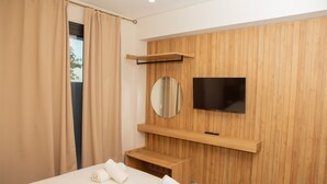 A hotel room with a bed, a TV mounted on a wooden wall, and a window with curtains.