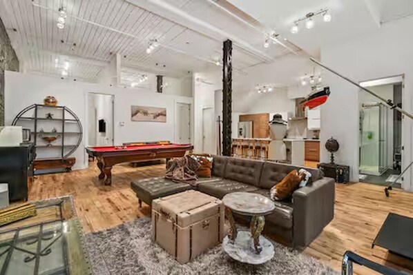 A spacious living room with a pool table, a leather sofa, and a staircase leading to an upper level.