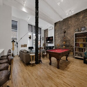 A spacious room with a pool table, a billiards rack, a sofa, a lamp, a bookshelf, and a television.
