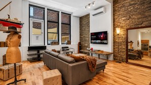 Una sala de estar moderna con un sofá modular, piso de madera, un televisor grande y una pared de piedra.
