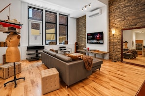 Ein modernes Wohnzimmer mit Ecksofa, Holzboden, großem Fernseher und Steinwand.
