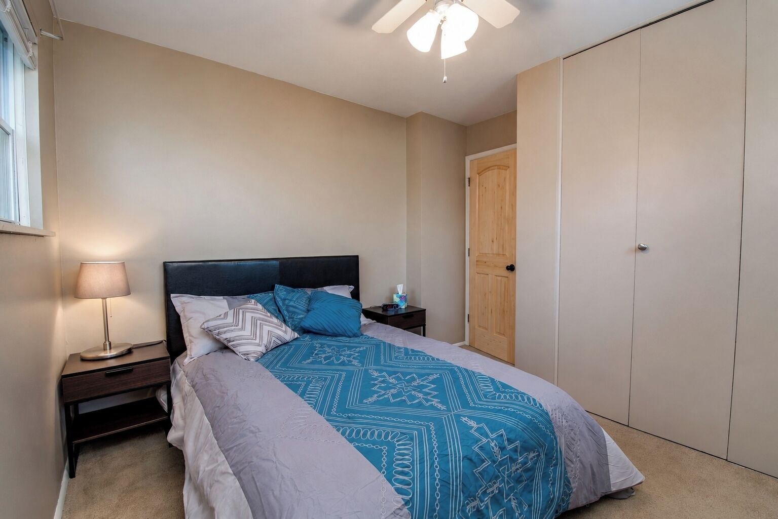Un dormitorio con cama, mesita de noche con lámpara, armario y una puerta.