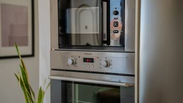A stainless steel oven with a digital display and control knobs, situated in a kitchen with a framed picture on the wall.