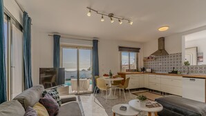 En moderne stue med sofa, sofabord og fjernsyn. Der er et spiseområde med bord og stole, samt et køkken med komfur og skabe.