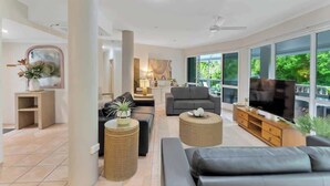 Amplia sala de estar con sofá, mesa de centro, televisor y ventanas grandes.