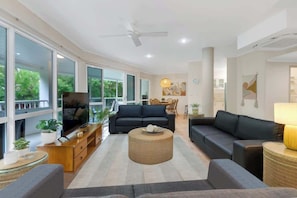 A spacious living room with a large TV, two sofas, a coffee table, and a ceiling fan.