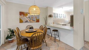 Comedor con una mesa redonda, sillas de madera, una lámpara colgante y una cocina al fondo.