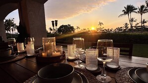 An outdoor dining setup with a sunset view, featuring a table set with plates, glasses, and candles.