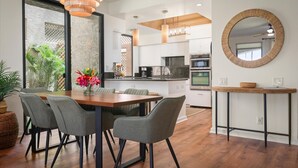 A modern kitchen with white cabinets, a wooden dining table, and a hanging light fixture.