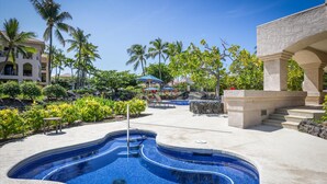 A swimming pool with a curved design, surrounded by palm trees and a building with a stone facade.