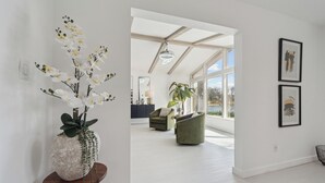 A spacious living room with a modern design, featuring a large window, a green sofa, and a decorative orchid arrangement. - Waterfront Paradise - 2 Lake Views in Prime Location (Battle Creek)