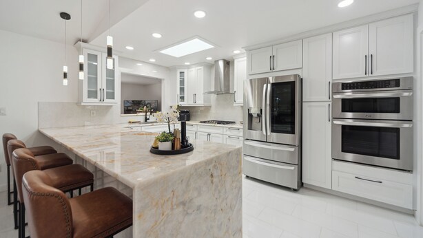 A modern kitchen with white cabinets, stainless steel appliances, and a marble island with bar stools. - Waterfront Paradise - 2 Lake Views in Prime Location (Battle Creek)
