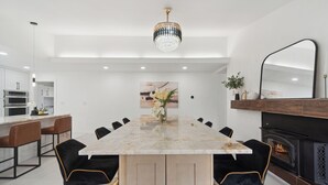 A modern dining area with a marble table, black upholstered chairs, a chandelier, and a fireplace. - Waterfront Paradise - 2 Lake Views in Prime Location (Battle Creek)