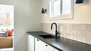 A modern kitchen with white cabinets, a black countertop, and a window above the sink. - The Kode | 2 Bedroom | Family Friendly Home (Drumheller)