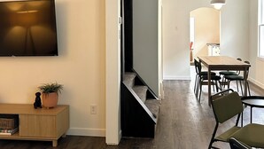 A modern living space with a flat-screen TV, a dining area with a table and chairs, and a staircase leading to another level. - The Kode | 2 Bedroom | Family Friendly Home (Drumheller)