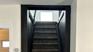 A carpeted staircase with a dark handrail and a door at the bottom. - The Kode | 2 Bedroom | Family Friendly Home (Drumheller)
