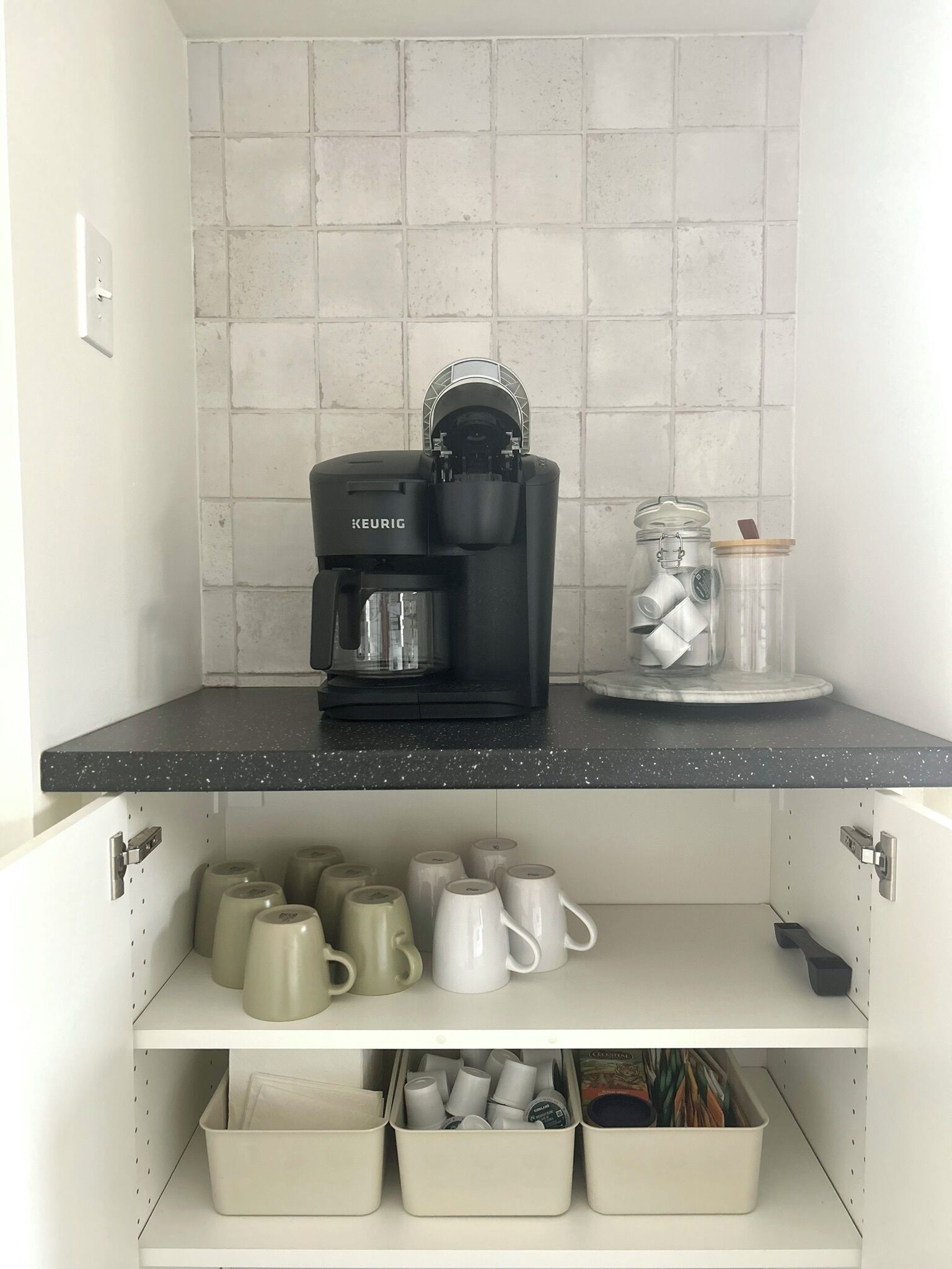 A kitchen with a Keurig coffee maker, a glass jar with a lid, and storage shelves with mugs and containers.