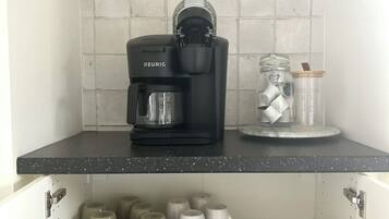 A kitchen with a Keurig coffee maker, a glass jar with a lid, and storage shelves with mugs and containers.